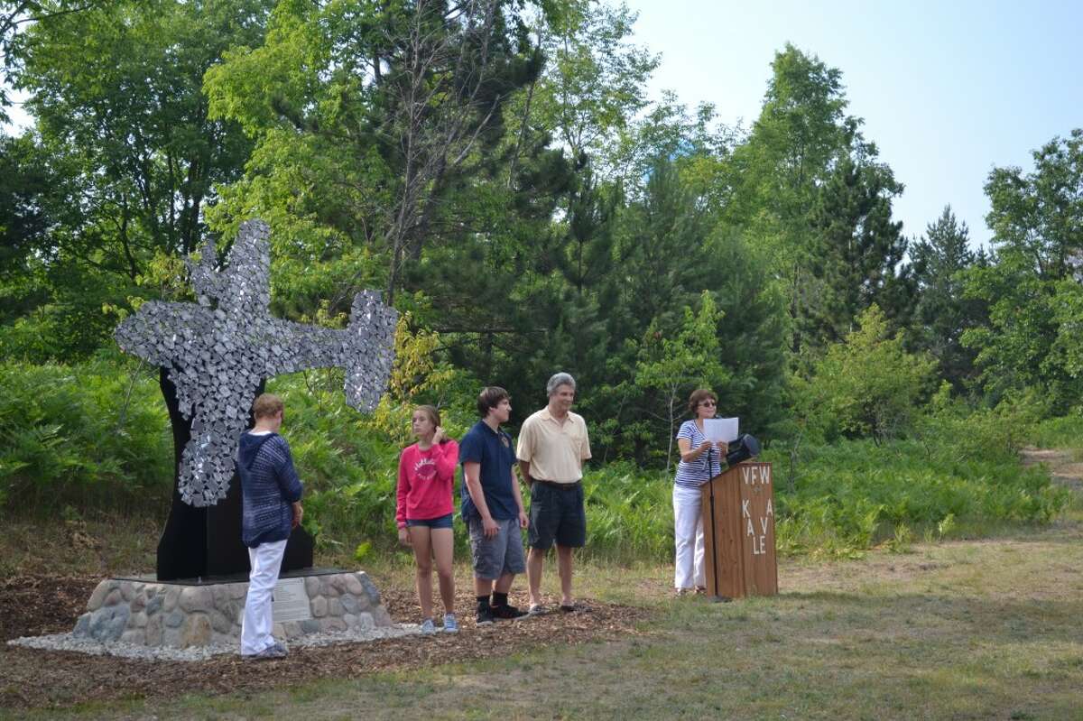 Cindy Asiala (RIGHT), president of the Kaleva Historical Society, dedicates the Robert E. Rengo Sculpture on Wednesday while (FROM LEFT) Laura Dorn, Brooklyn Dorn, Emil Rengo and Phillip Rengo, the children and grandchildren of Robert Rengo, look on. (Meg LeDuc/News Advocate)