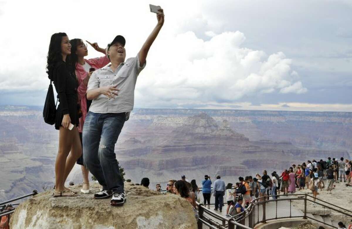 FILE - In this Aug. 2, 2015, file photo, tourists Joseph Lin, Ning Chao, center, and Linda Wang, left, pose for a selfie along the south rim at Grand Canyon National Park, Ariz. The Grand Canyon is celebrating 100 years as a national park in 2019. President Woodrow Wilson made the designation in 1919. But Teddy Roosevelt is credited for preserving the natural wonder as a game reserve and a national monument. (Emery Cowan/Arizona Daily Sun via AP, File)