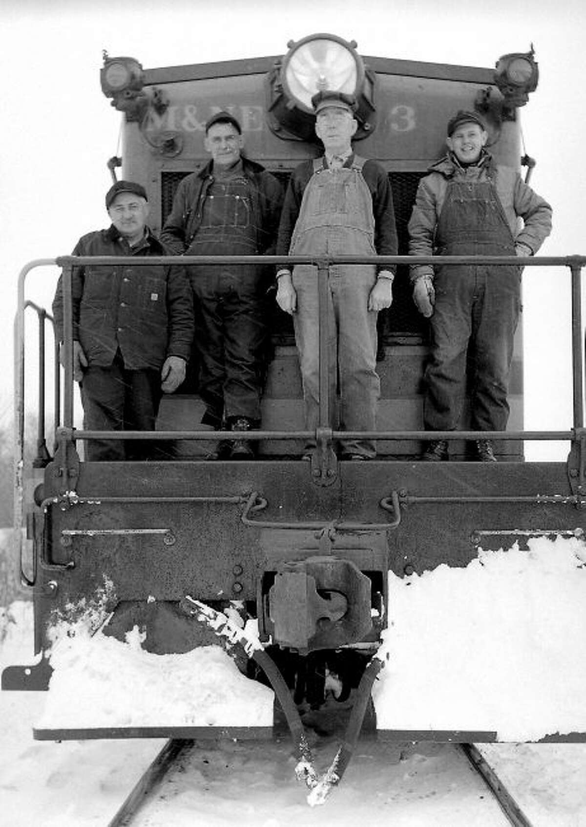 Workers from the M&N.E. railroad stand on the front of their engine in this 1950s photograph.