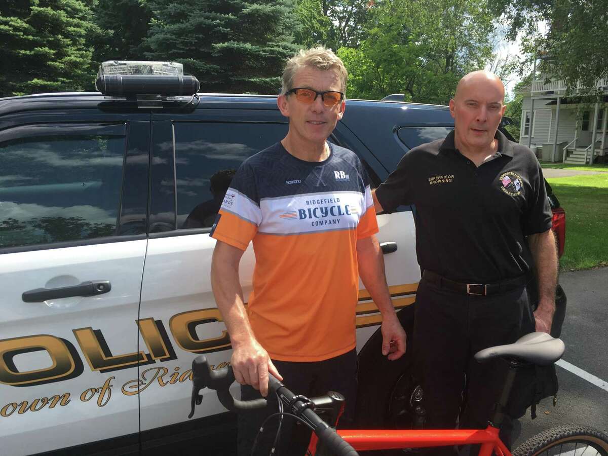 Cyclist Ciaran Carruthers (left) and police dispatcher Bill Browning (right) in front of a Ridgefield Police cruiser Wednesday, July 24. Browning is helping Carruthers raise funds for the annual Pan-Mass Challenge bicycle ride, which sees some 6,700 riders converge on Sturbridge Mass. to raise money for the Dana-Farber Cancer Institute.