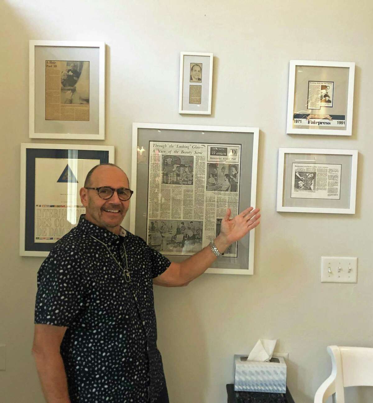 Charles Tuozzoli points to framed articles about his 1974 lawsuit, where he won the right to cut both men's and women's hair.