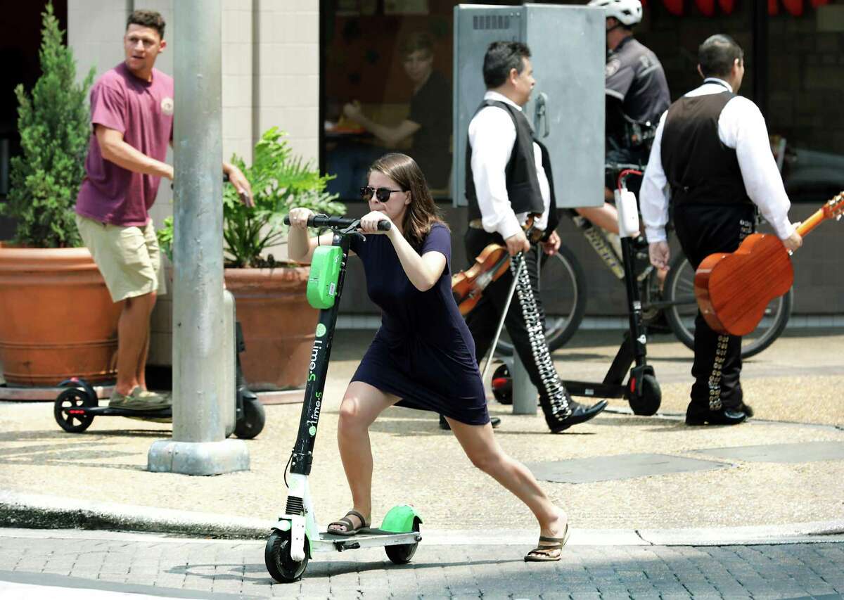 A woman and and man, left, ride scooters across W. Commerce St. on the side walk at Presa St. on Thursday, May, 30, 2019. At the City Counsel meeting city leaders voted to ban riding scooters on sidewalks.