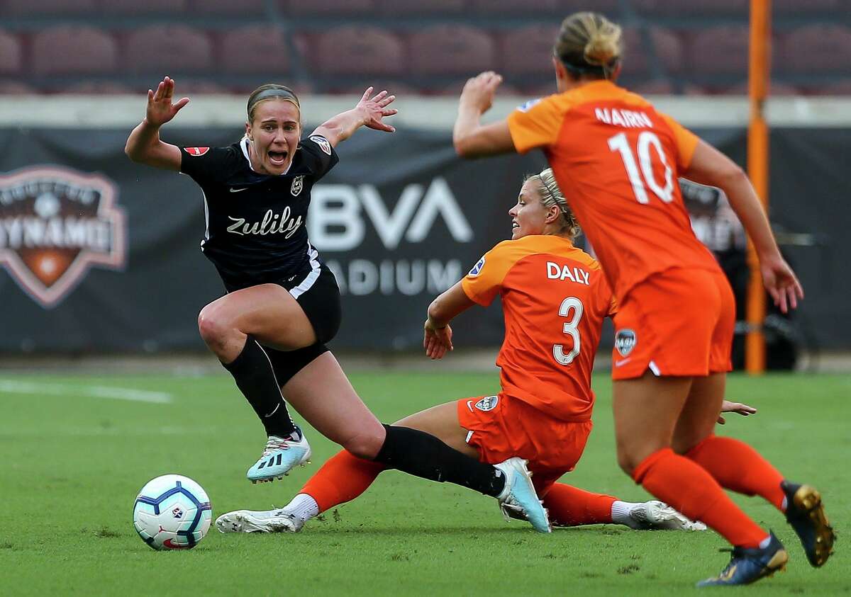 Reign FC midfielder Bev Yanez, left, goes down as she is challenged by Dash forward Rachel Daly (3).