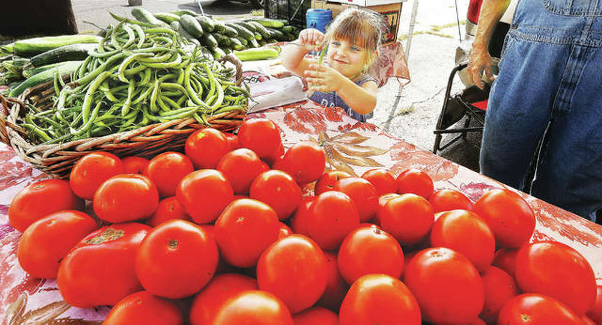 Marley Beilsmith, 4, of Jerseyville, plays with a green bean as she helps her grandfather, Bob Sancamper, at his produce stand in the Alton farmer’s market on the parking lot at the foot of Henry Street in Alton. Despite a rainy start to this year’s season, vendors at local farmers’ markets say they are having a good year.