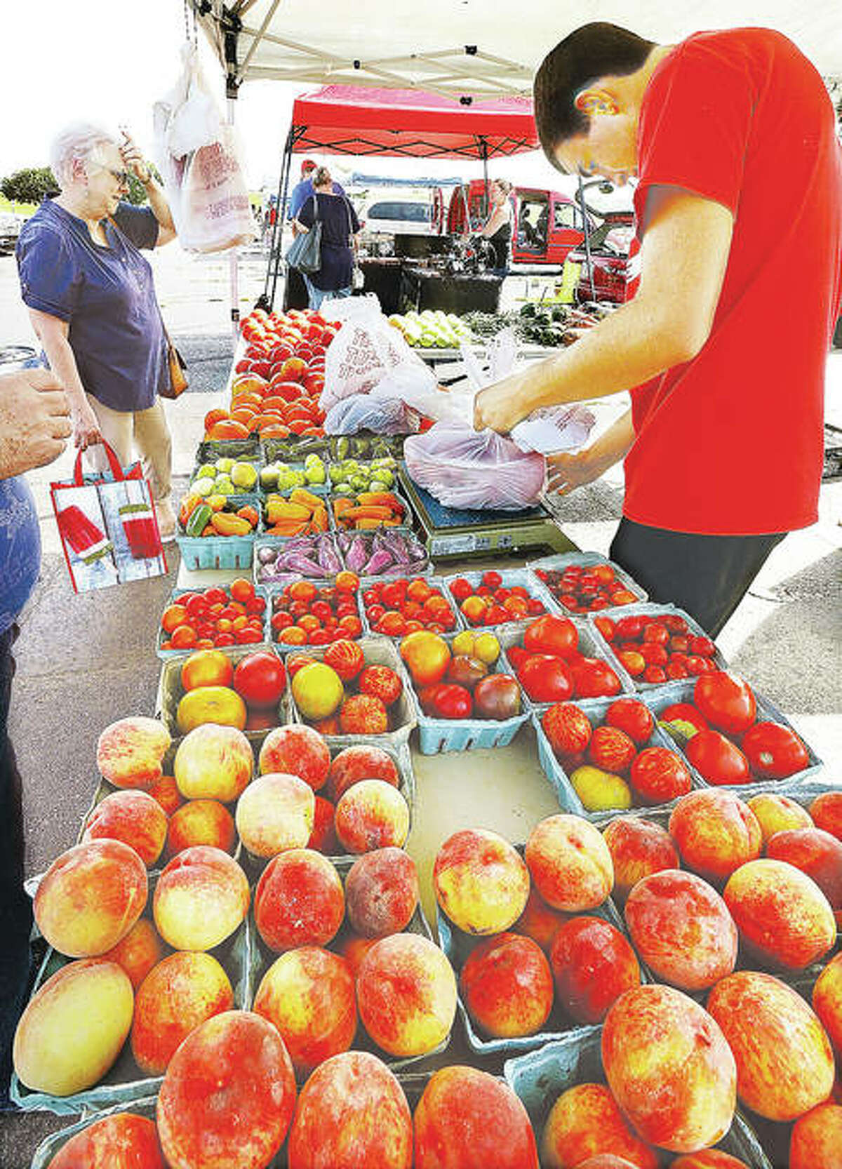 Jo Ellen Johnson, left, of Grafton, looks over the wares at the Baalman’s Produce stand at the Alton farmer’s market as Drew Baalman, right, weighs up a customer’s fresh fruit and veggies.