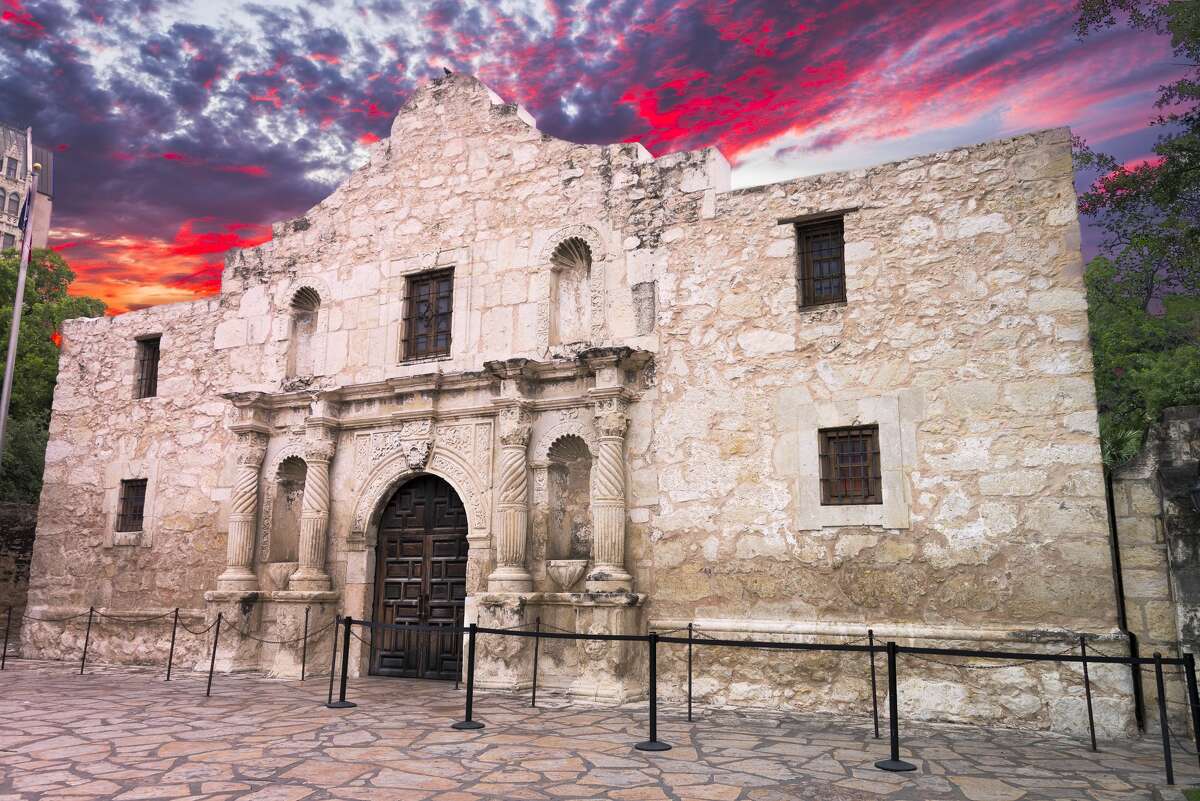 Exterior view of the historic Alamo featuring a glowing crimson sunrise sky in the background.