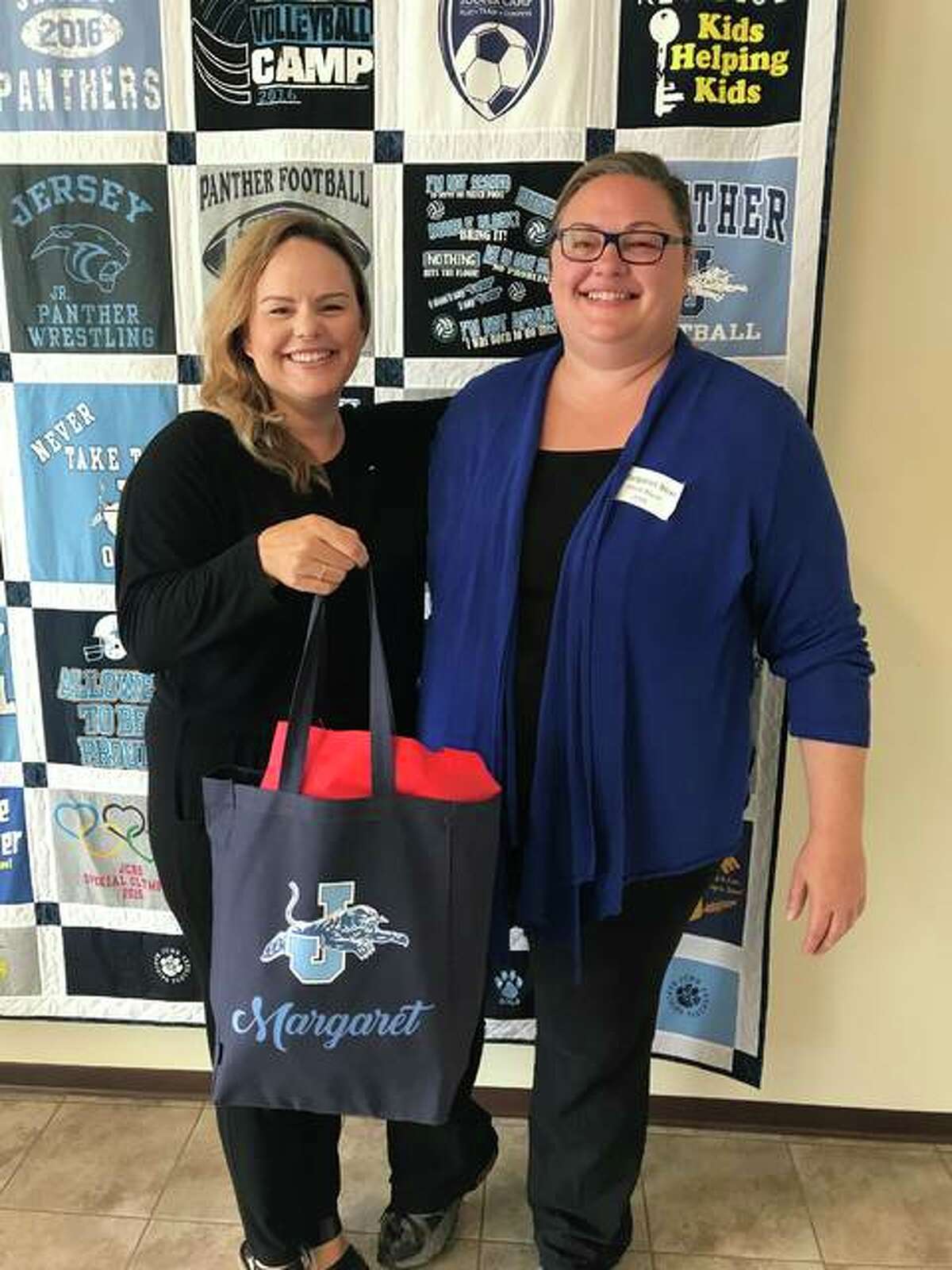 Jersey County Business Association Director Beth Bear presents a “Welcome Bag” to her sister, Margaret Bear, the new choral director at Jersey Community High School. Jersey County businesses recently provided the bags to 24 new teachers.