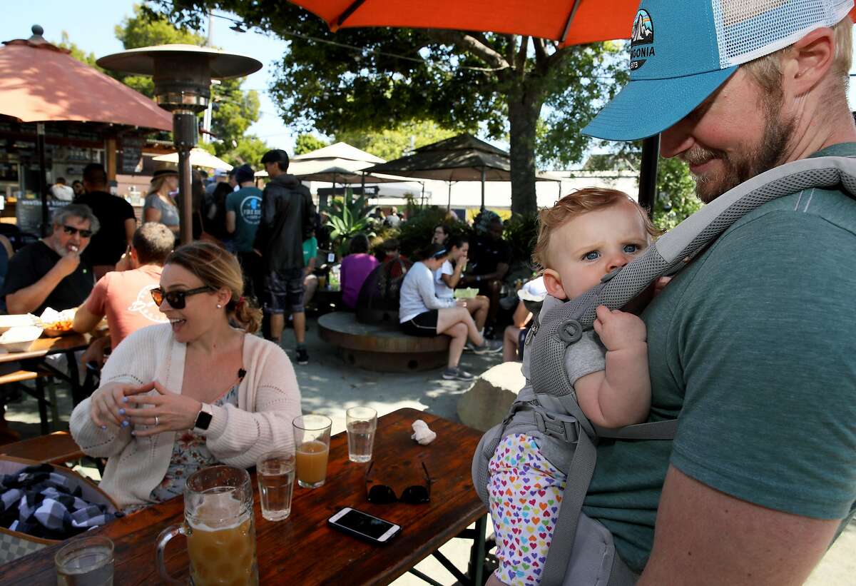 Shawn Swim (right), 33, looks at his daughter Reese, 8 months, as his wife Allison (left), 33, all of Berkeley, converses with visiting friends at Westbrae Biergarten, located at 1280 Gilman St., in Berkeley, Calif., on Saturday, August 10, 2019.