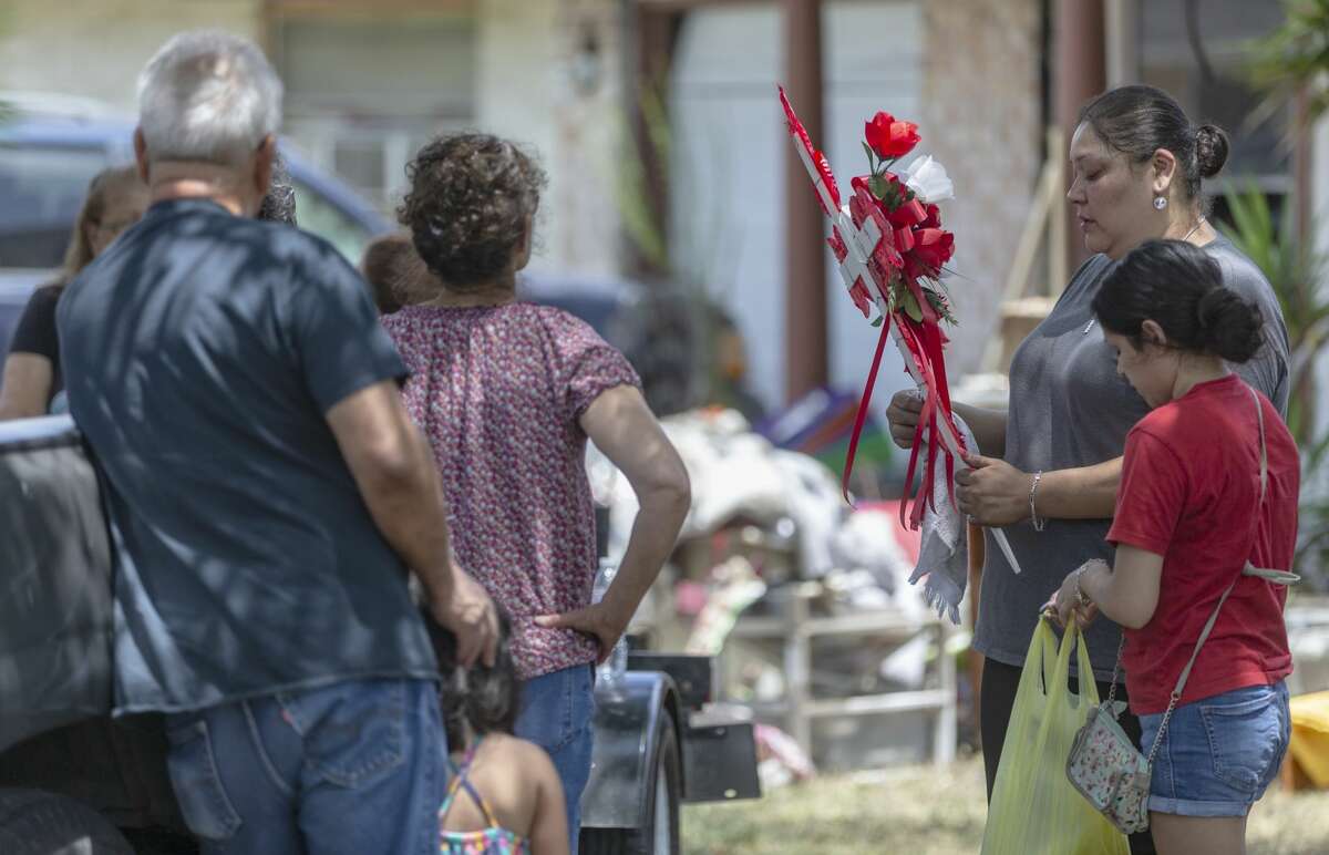 Christina Gonzalez, second from right, looks Tuesday, Aug. 6, 2019 at a flower-adorned cross outside the home in the 7500 block of Dream Valley where a triple homicide-suicide occurred Monday evening.