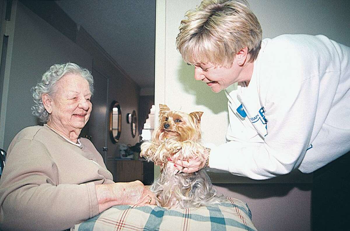 Seniors can benefit greatly from pet therapy. Here, a volunteer, right, introduces Annie, center, to a retirement home resident.