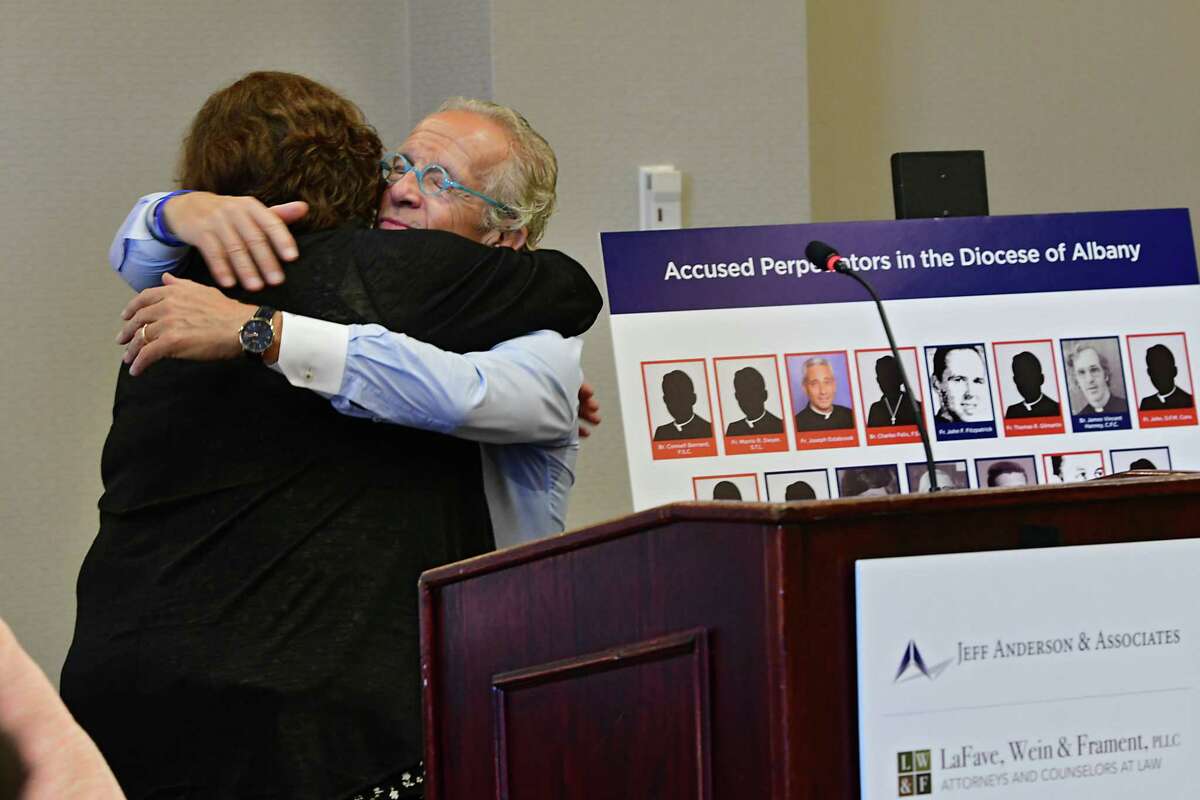 Survivor Jeanne Marron hugs attorney Jeff Anderson next to board of perpetrators in the Diocese of Albany during a press conference where Anderson announced 20 lawsuits filed against the Albany Diocese on the first day the Child Victims Act at the Hilton Albany on Wednesday, Aug. 14, 2019 in Albany, N.Y. The act allows a one-year period for claims to be filed regardless of the age of the plaintiff. Survivor and advocate Bridie Farrell stands at right. (Lori Van Buren/Times Union)