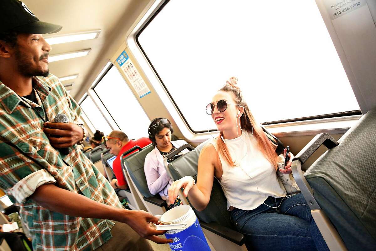 Tone Oliver (l to r) accepts a donation fromBrittany Pilgram of Oakland after performing on a BART train on Wednesday, August 14, 2019 in Oakland, Calif.