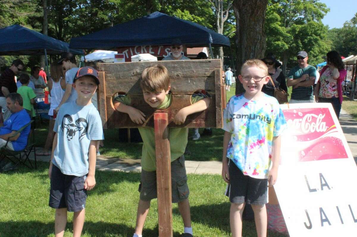 IN THE STOCKS: Hunter Reid (center) finds himself in the Lake Ann “jail” during the Homecoming event on July 6. Keller Reid (left) and Mason Richardson (right) keep watch over him. (Photos/Bryan Warrick)