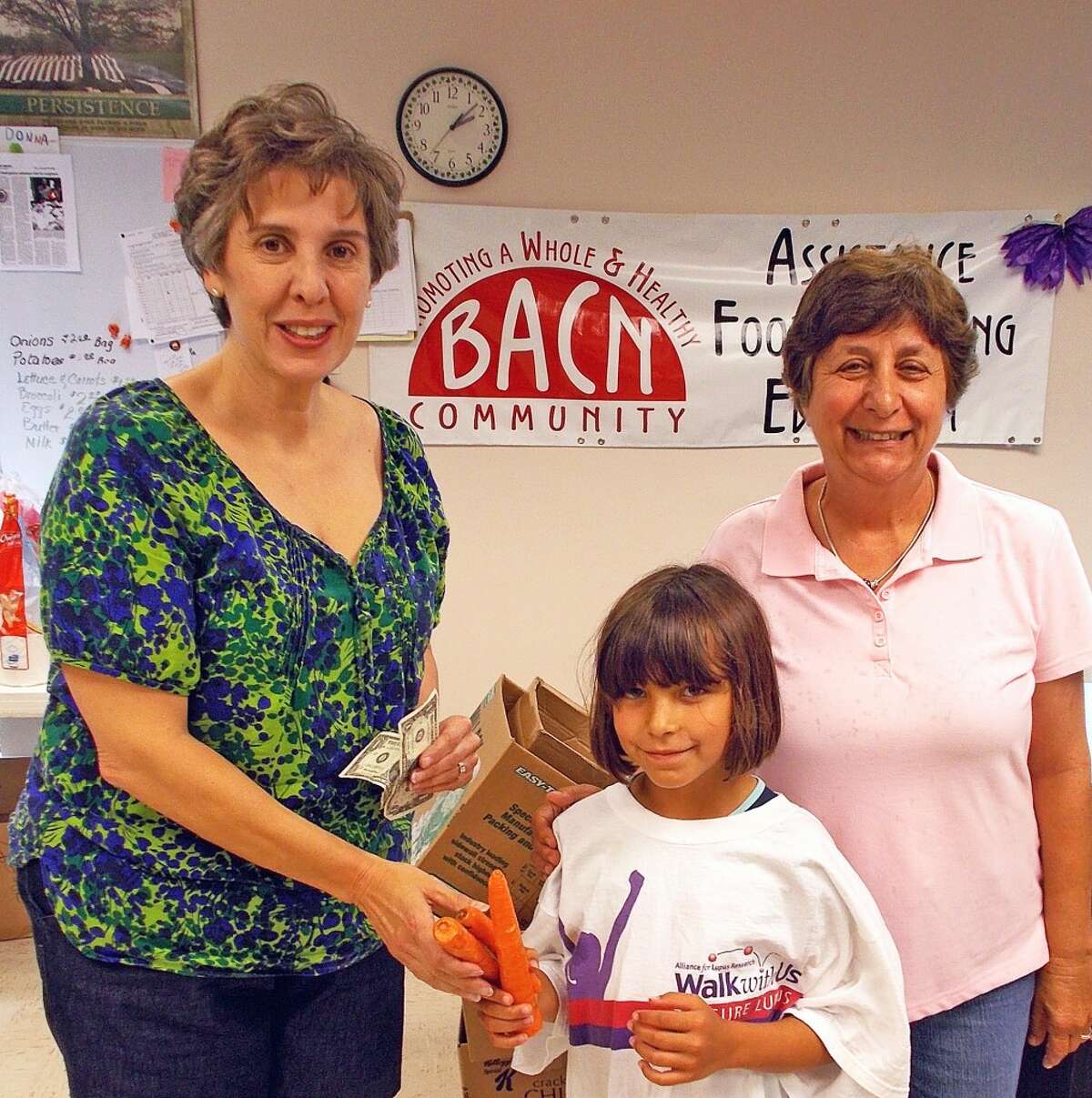 CHARITY: Gerri VanAntwerp, BACN Executive Director accepts carrots and cash from 8 year old Gracie who grew and sold her vegetables at Grow Benzie this summer. Gracie donated 10 percent of her sales and picked BACN as her charity to support. (Courtesy photo)