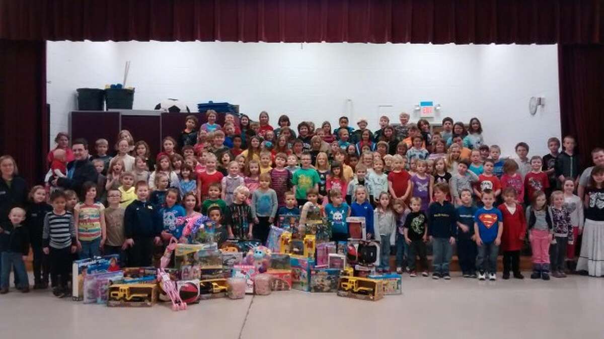 GIVING BIG FOR CHRISTMAS: The entire student population of Betsie Valley Elementary, along with Ben and Amy McRae, owners of The Corner Toy Store of Frankfort, in front at left, stand with more than $700 worth of toys donated to Toys for Tots. (Courtesy photo)