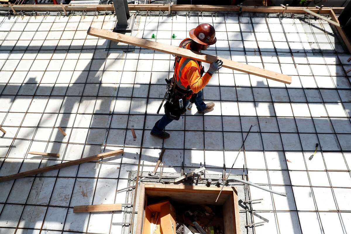 A worker carries a 2x4 for a concrete form at the construction site of a 20-story residential building going up on the 1700 block of Webster Street in Oakland Calif., on Wednesday, July 17, 2019. Oakland�s downtown has long been revered as hip, electric and historic. Five years ago, the area underwent a transformation minority-owned nail salons shuttered and were instead replaced by hipster bike shops. Now, stores and other businesses are facing a similar transformation as cranes dot the skyline and 20-story buildings go up. One downtown block, near 17th and Webster, is a microcosm of the change that�s coming once again to downtown Oakland. There are three big development projects currently under construction on that block - two of which will have 20-story towers.