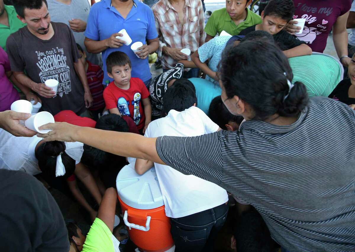 Migrantes se reúnen para recibir agua ofrecida por religiosos voluntarios en las oficinas de Inmigración de México en el Puente Internacional Número 1 en Nuevo Laredo, México, el jueves 15 de agosto de 2019.