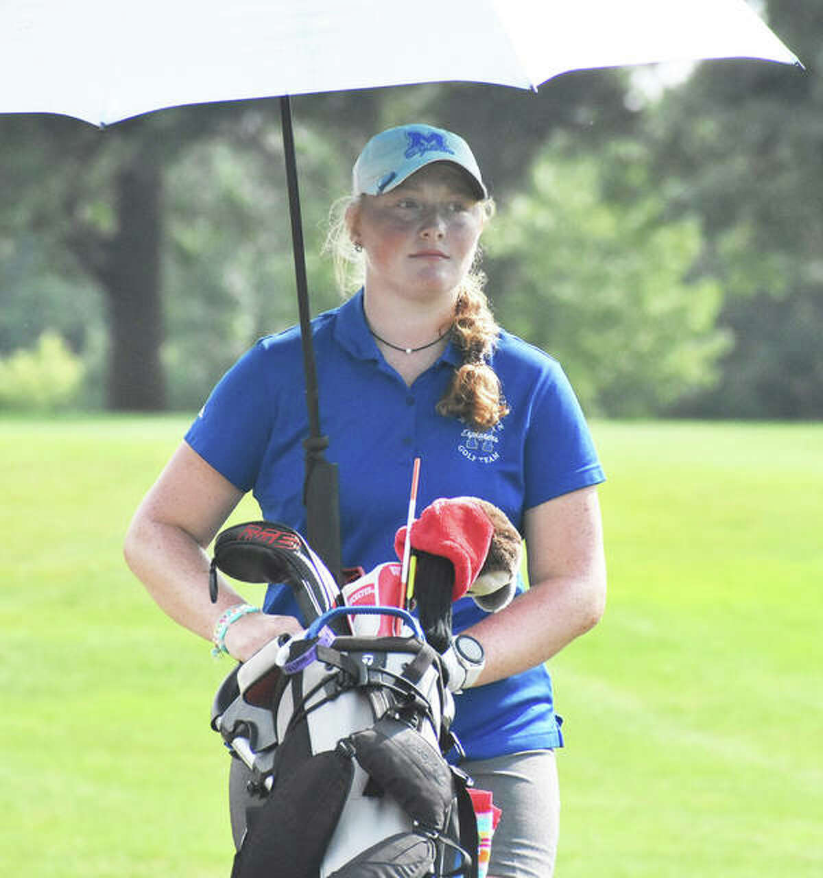 Marquette Catholic’s Gracie Piar finds some shelter from the sun under an umbrella between shots Friday at the Prep Tour Showcase at Hickory Point in Forsyth. Piar shot 75 to tie for fifth.