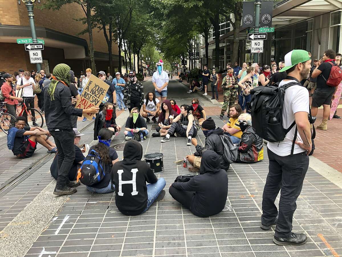 Anti-fascist counter-demonstrators sit down in Portland, Ore., Saturday, Aug. 17, 2019. Not all who gathered Saturday were with right-wing groups or antifa. Authorities closed bridges and streets to try to keep the rival groups apart. The city's mayor said the situation was "potentially dangerous and volatile," and President Donald Trump tweeted "Portland is being watched very closely." As of early afternoon, most of the right-wing groups had left the area via a downtown bridge. (AP Photo/Gillian Flaccus)