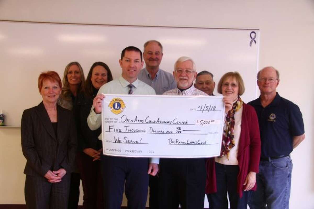 Jim Eddinger (front left) receives a check donation from Big Rapids Lion Club President Tom Samuel (front right) for the Open Arms Child Advocacy Center, surrounded by Lions Club members and members of the child advocacy development team. (Pioneer photo/Emily Grove)