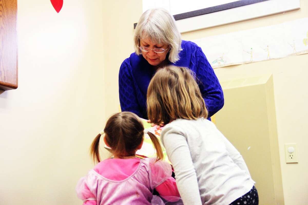 YOUNG LISTENERS: Two children not yet old enough for school enjoy hearing Candy Derevage — known as Mrs. D — read a story. Derevage has read to many children in the Reed City community through her 20 years at Reed City Library. (Herald Review photo/Sarah Neubecker)