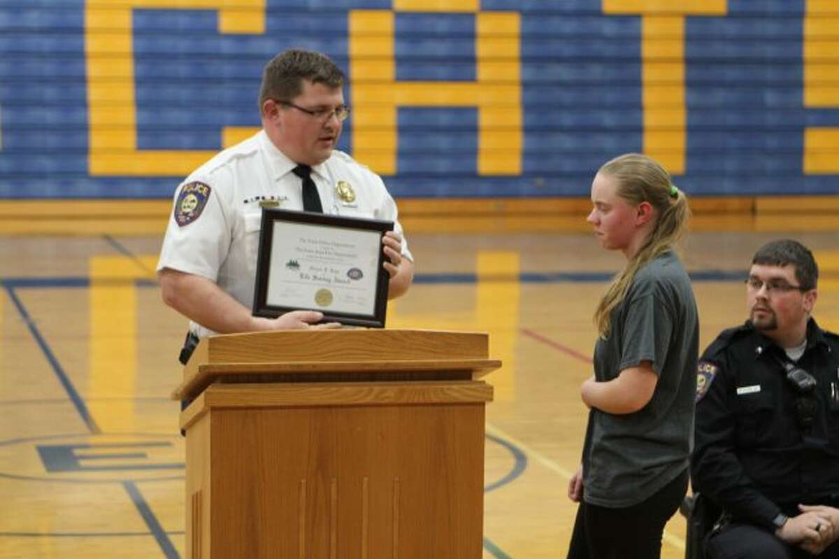 Evart High School senior Nichole Roys (right) stands as she is recognized for her quick thinking and actions on Tuesday, Dec. 4, when she performed the Heimlich maneuver on a choking fourth-grader. She received a plaque for her services on Thursday, Dec. 13, from Evart Police Department Chief John Beam. (Herald Review photo/Meghan Gunther-Haas)