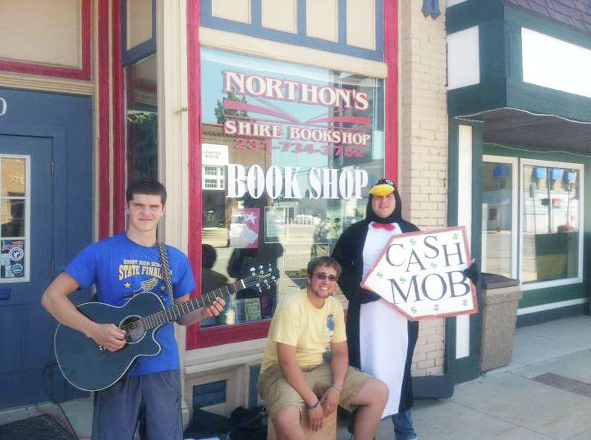 CashMob: Cash Mob Mondays volunteers (from left) Antonio Militello, AJ Weinberg and Chris Moore help draw people into Northon's Shire Bookshop with music during last year's event in Evart. This year, Cash Mob Mondays will begin on June 3 at B.C. Pizza.