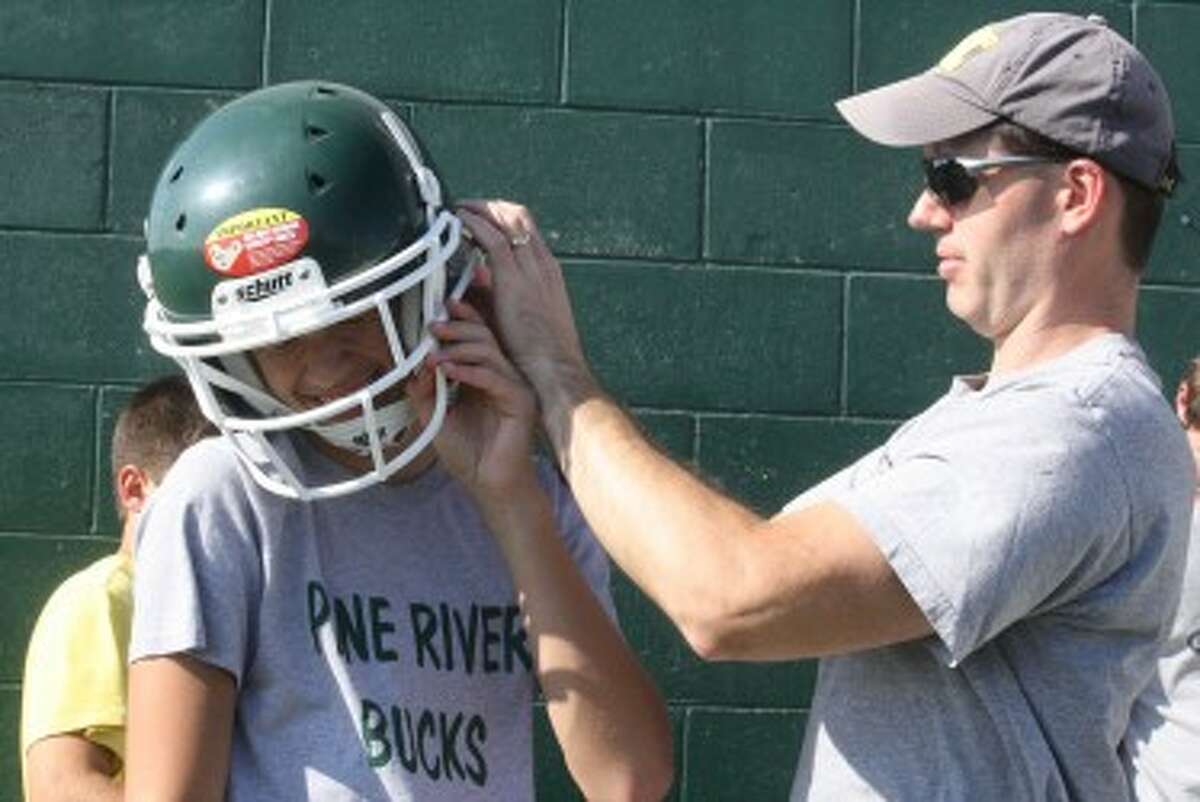 IN A SNAP: (ABOVE) Hunter Esiline, an eight-grader at Pine River, gets help from his dad, Todd Esline, in getting the helmet to fit at the Pine River football camp on Monday. (Pioneer photos/John Raffel)