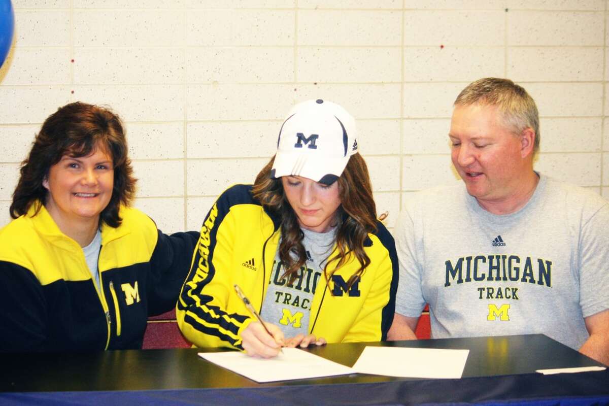 TIME TO SIGN: Vikki (left) and Brent Michell watch as their daughter, Sami Michell of Reed City signs her national letter to run track at Michigan. (Herald Review photo/John Raffel)