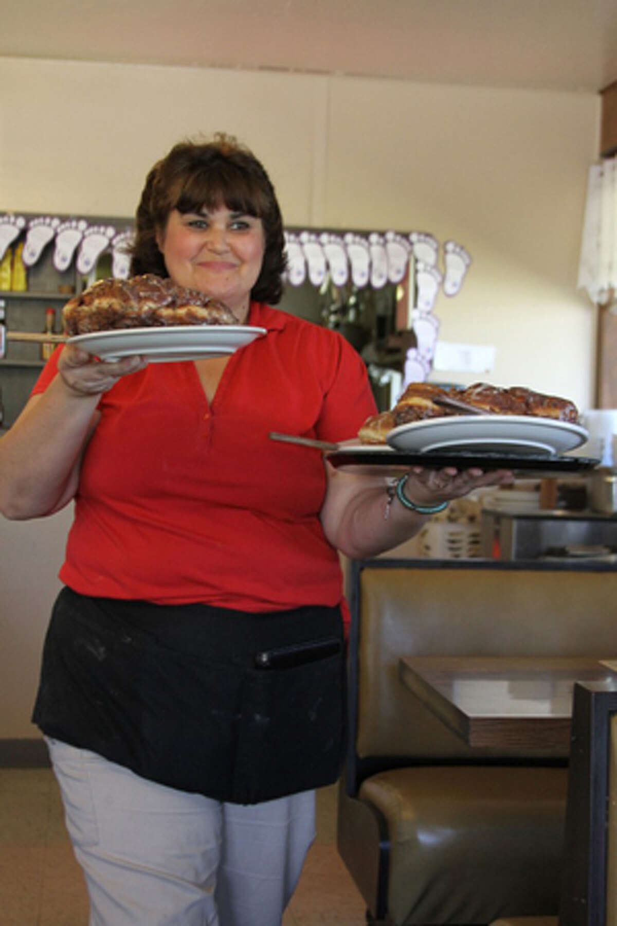 ORDER UP: Laurie Kogler serves up a trio of H&D Chuckwagon’s signature oversized doughnuts. The Reed City-based family-style restaurant prepares about 150 of the large baked goods each day. (Herald Review photos/Jonathan Eppley)