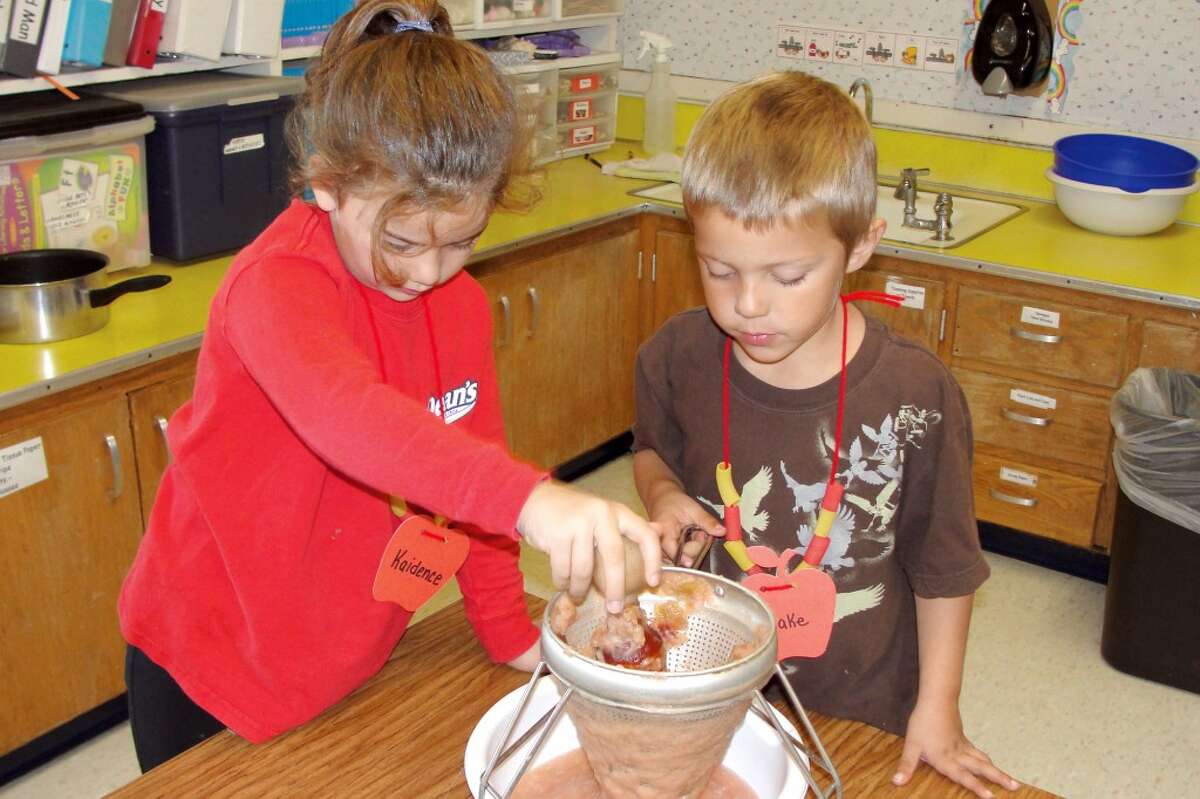APPLESAUCE: Kaidence Reid and Blake Jennings work the softened apples through the sieve to make applesauce. (Herald Review photo/Shannon Hartley)