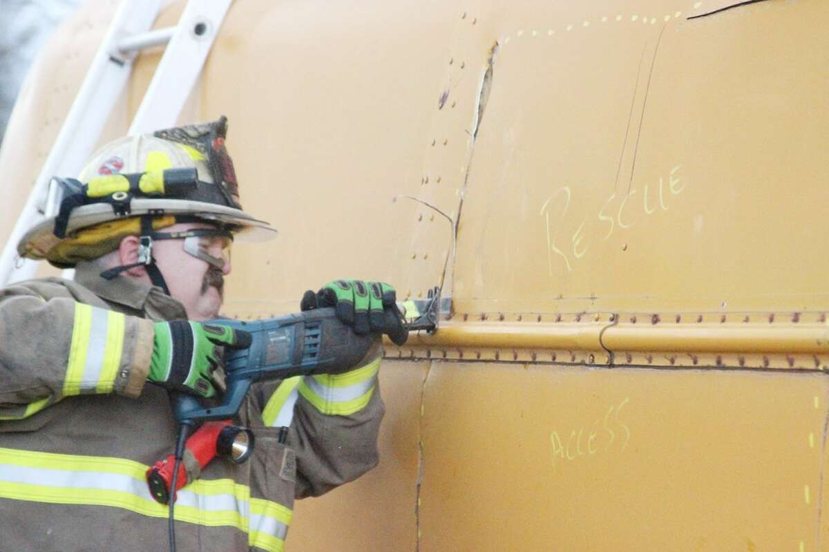 RESCUE ACCESS: A firefighter cuts through the top of a turned-over school bus during a training exercise on Saturday in Reed City. The words “rescue access” and a dotted line outline where firefighters had to cut to safely enter the bus without injuring any passengers or cutting through roof support beams.