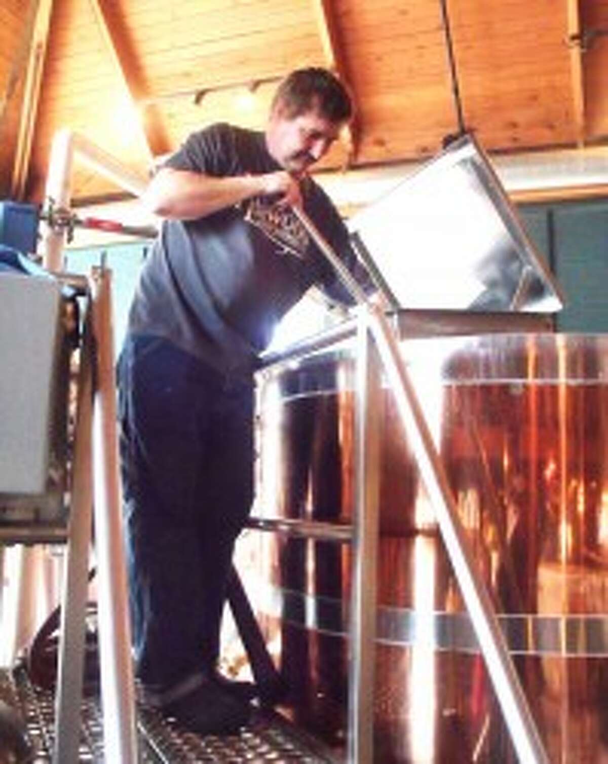 BREWMASTER: Steve (Konrad) Conner, head brewer at Redwood Brewing Company, stirs the mash as part of the preparation of a new batch of cream stout. Conner earned a silver medal in the Great American Beer Fest national competition for this brew. Below, Redwood Lodge proudly displaysw a banner hailing Conner’s success. (Herald Review photo Jim Crees)