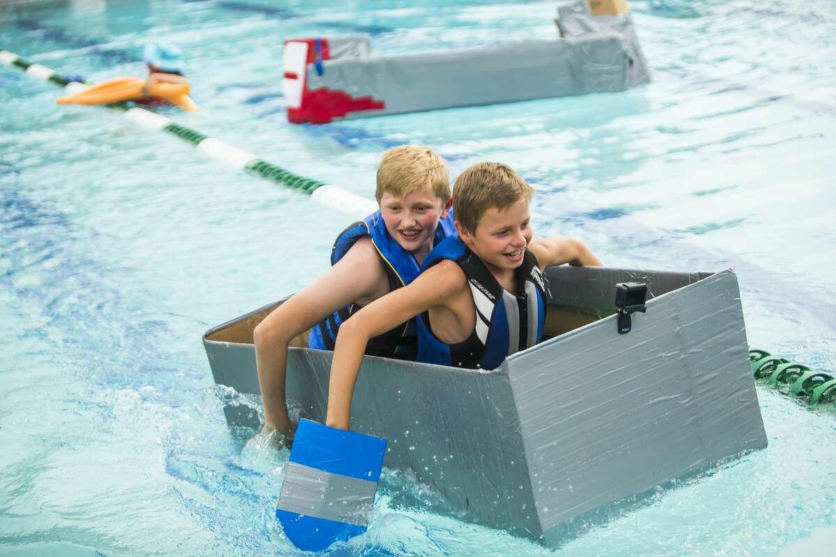 Matthew McGaugh, 11, front, and James Glackin, 13, back, race their boat across the swimming pool at the Midland Country Club during a cardboard regatta on Tuesday, Aug. 20, 2019. (Katy Kildee/kkildee@mdn.net)