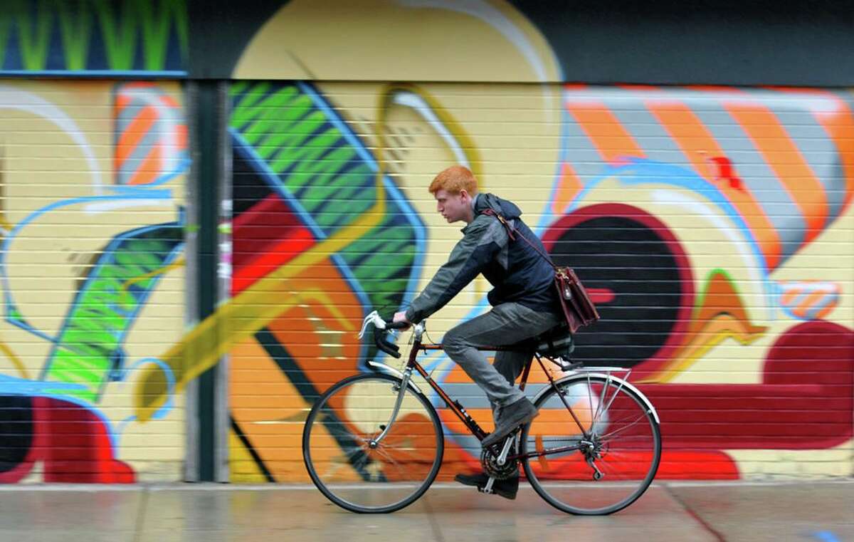 A cyclist rides through the light rain along Crown Street past street art near the corner of College Street.