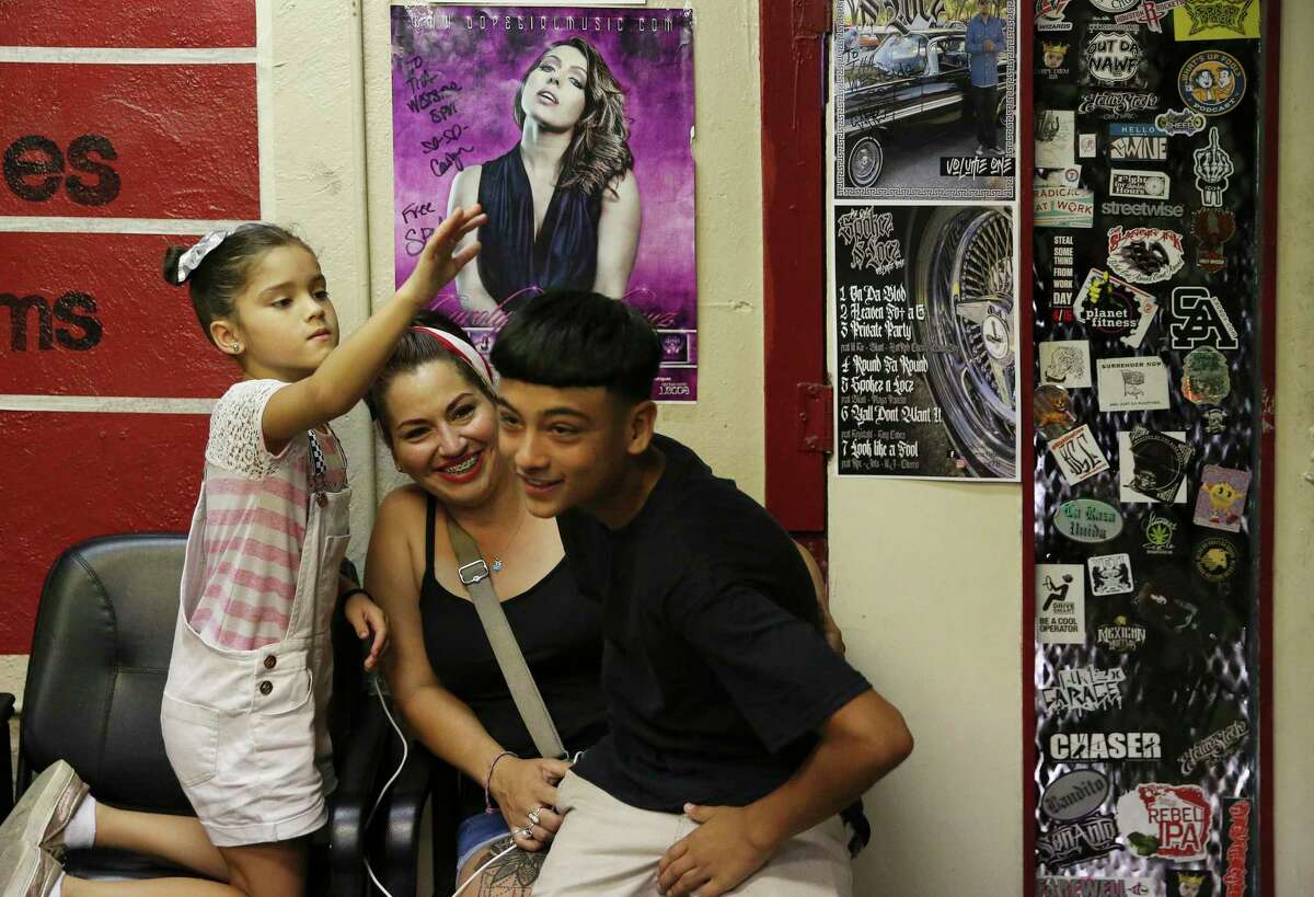 Avery Robles, 8, reaches out to touch the hair of her older brother, Reece Robles, 13, after his haircut as their mother, Nancy Ramirez looks on at Jesse "Latino" Barrientes' barbershop, Tha Westside Spot, on Saturday, Aug. 10, 2019. For the past several years, Barrientes has organized a giveaway of backpacks and school supplies for neighborhood children with the help of friends and neighbors who donated the school materials and backpacks. Nestled in the heart of the West Side, Barrientes believes strongly that his community doesn't receive the attention it deserves. But he just as strongly believes in his motto: Ain't nobody gonna help the barrio unless the barrio helps itself." On Saturday, school children and their parents trickled in to pick up a backpack or school supply and maybe get a top-notch haircut from Barrientes. Occasionally, a donor carrying bags of pencils, notebook paper, crayons and a new backpack would also stroll in to help the barber's cause as a mother with her three boys wait their turns to get their hair cut. (Kin Man Hui/San Antonio Express-News)