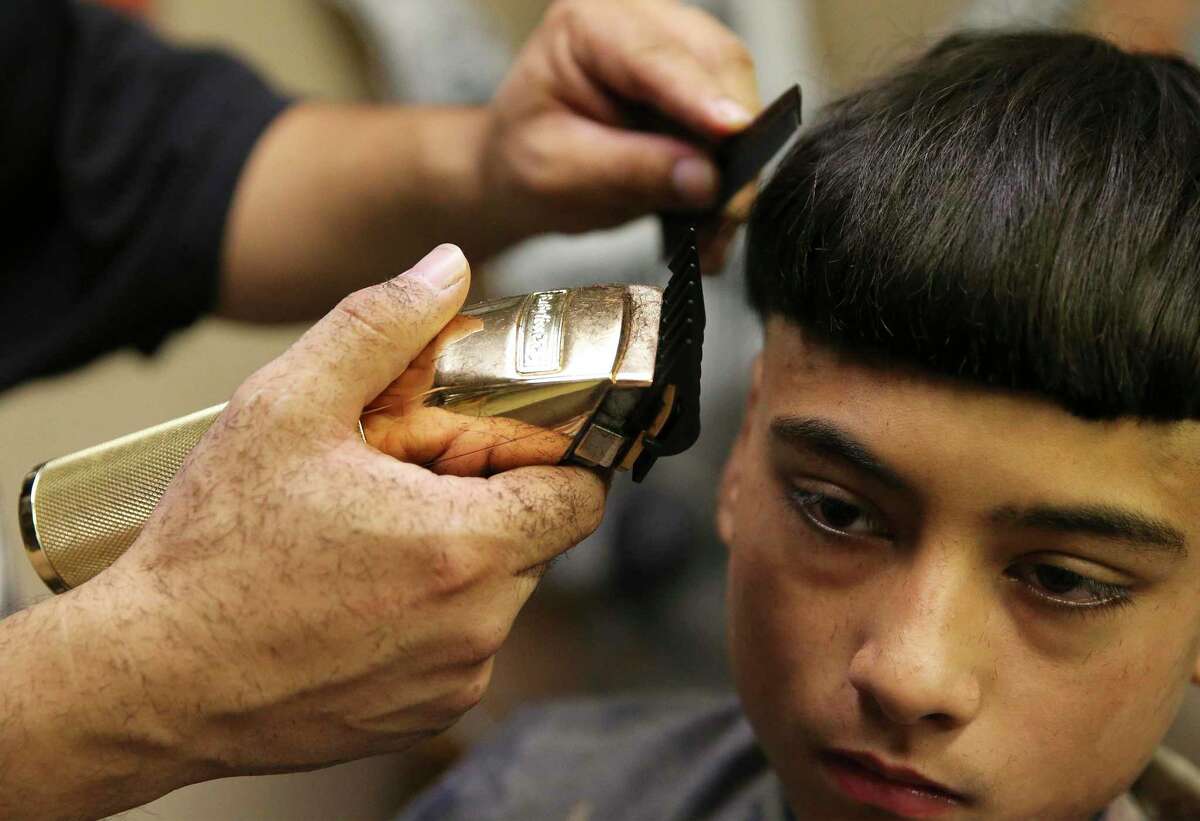 Jesse "Latino" Barrientes, owner of hair stylist and hip-hop shop Tha Westside Spot, works on haircuts for Reece Robles, 13, while also delivering backpacks and school supplies for neighborhood kids.