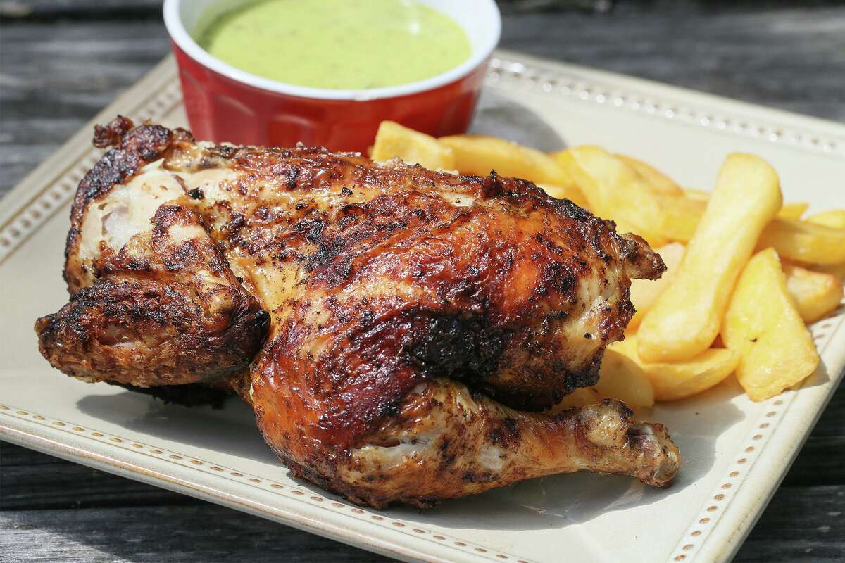 A finished Peruvian chicken half paired with traditional fries and a guacamole salsa for dipping.