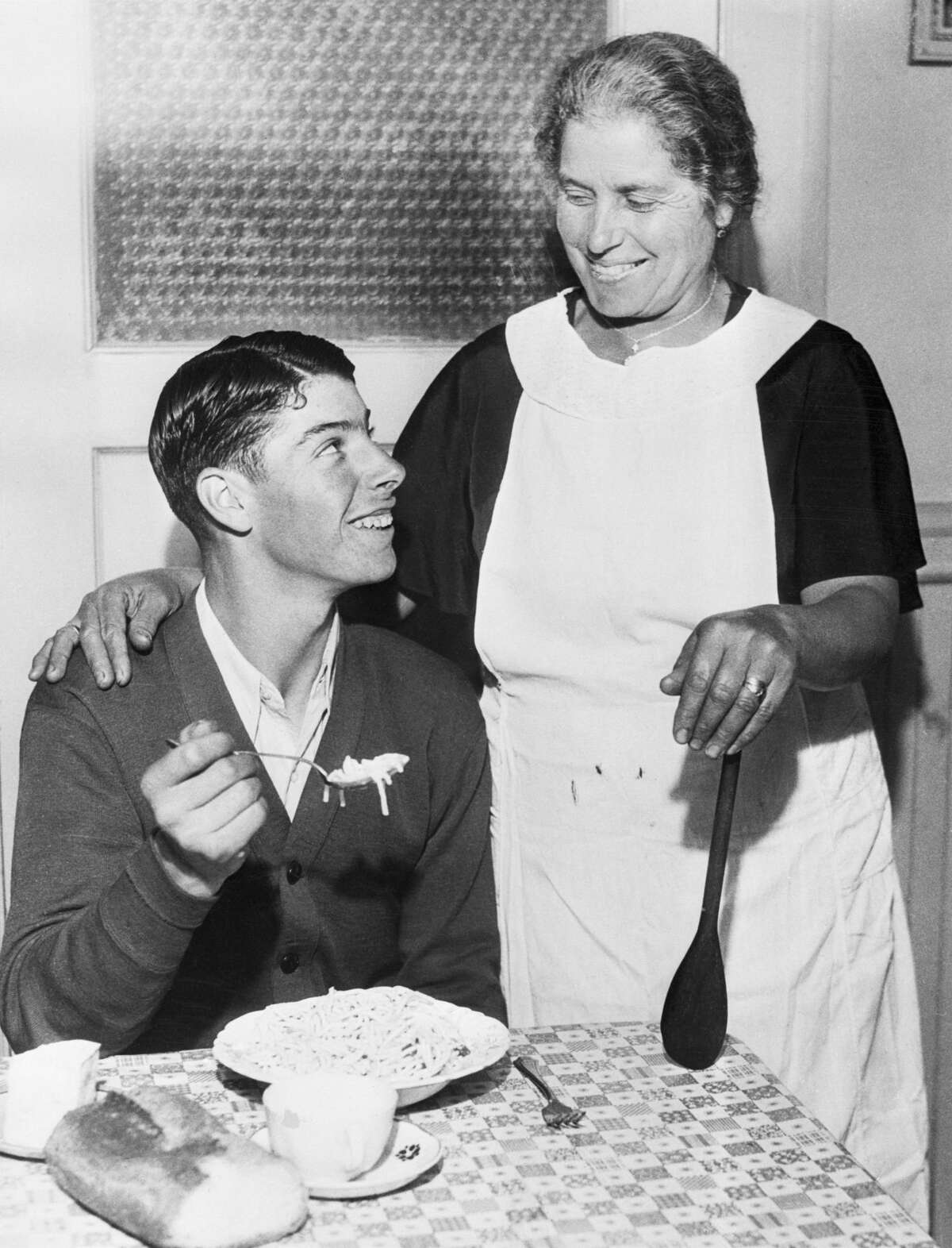 Young Joe DiMaggio eating spaghetti while his mother Rosalia looks on.