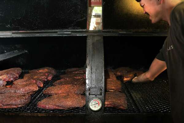 Dusty Dworak, pit hand and slicer at 2M Smokehouse, moves seasoned ribs, right, and briskets, left, in a custom-made smoker.