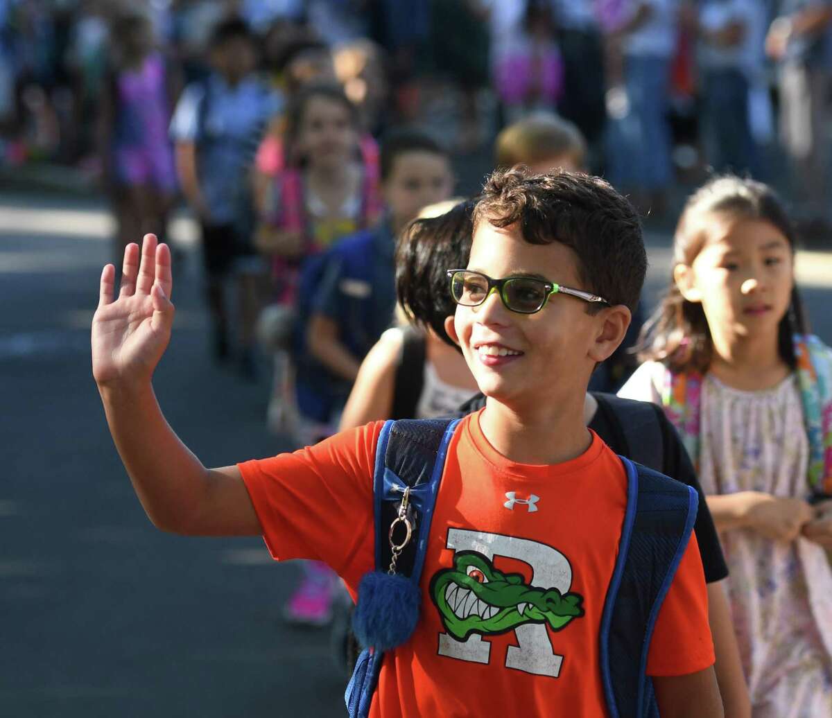 Third-grader Nash Goodman waves to parents in the crowd while walking with his new classmates in the Parade of Learners on the first day of school at Riverside School in the Riverside section of Greenwich, Conn. Thursday, Aug. 29, 2019.