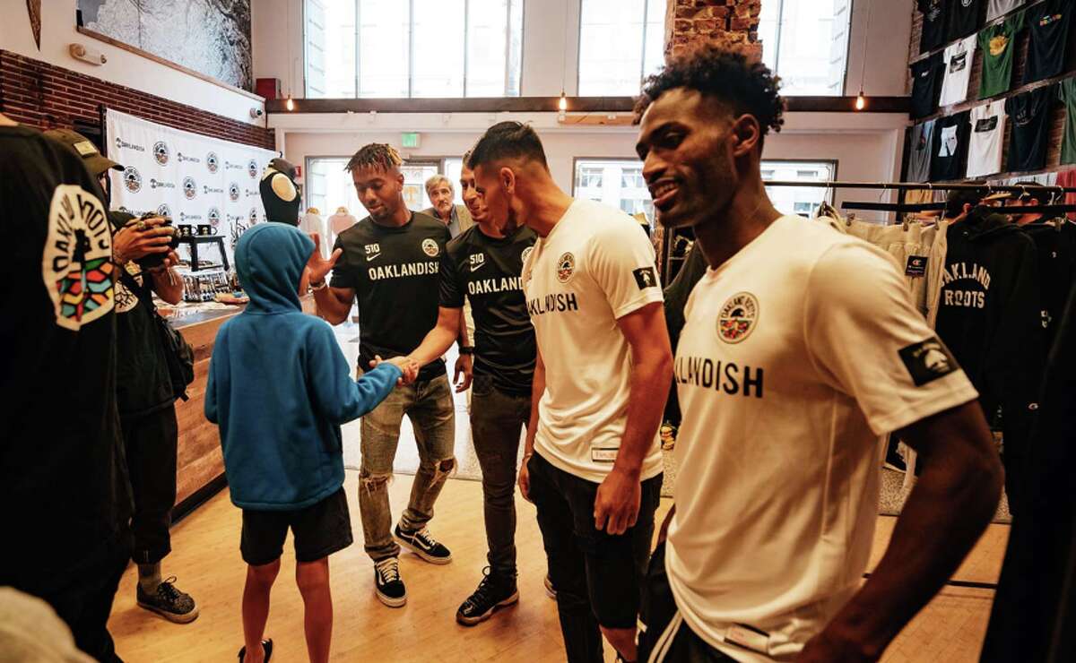 Oakland Roots players (left to right) Benji Joya, Devante Dubose, Julio Cervantes, and Yohannes Harrish talk with a young fan at the Roots jersey unveiling at Oaklandish's downtown Oakland store on June 28, 2019.