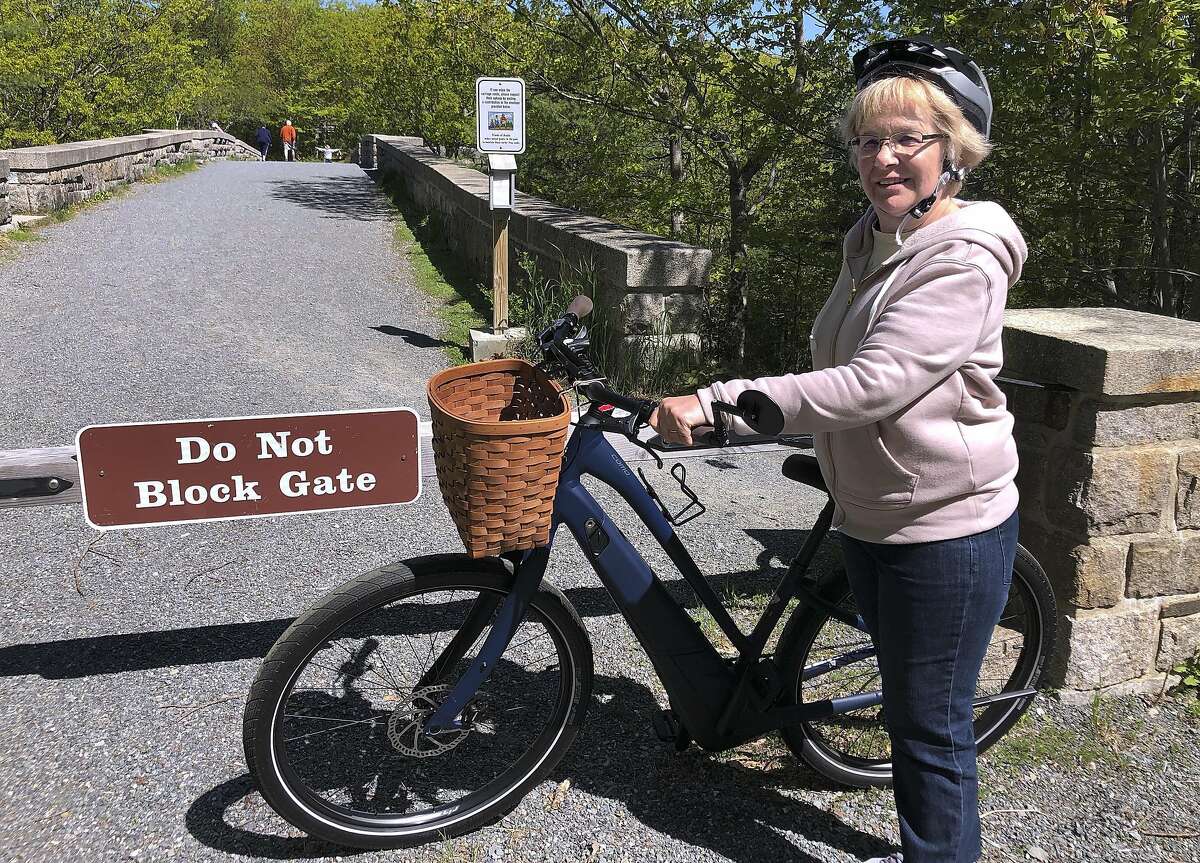 FILE-In this June 8, 2019 file photo, Janice Goodwin stands by her electric-assist bicycle at a gate near the start of the carriage path system where bikes such as her are banned inside Acadia National Park, in this photo June 8, 2018, in Bar Harbor, Maine. Interior Secretary David Bernhardt signed the order on Thursday allowing motorized electric bicycles into national parks and other public lands.