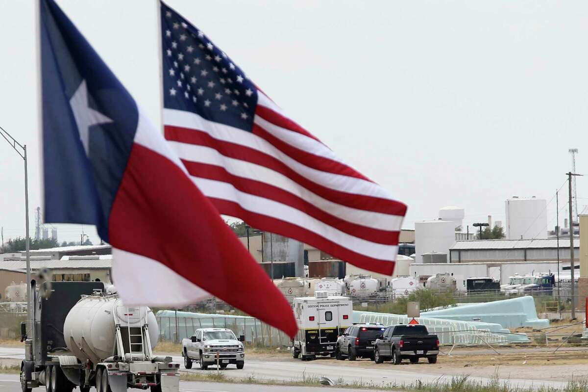 Law enforcement vehicles are seen behind the U.S. and Texas flags hanging from tow trucks along IH-20 near the Odessa, Texas city limits, Sunday, Sept. 1, 2019. Seth Aaron Ator, 36, of Odessa, is suspected of killing seven people an injuring 19 in a shooting spree in Odessa on Saturday. Before the rampage, Ator was stop along IH-10 between Odessa and Midland by a Texas Department of Public Safety trooper for a traffic violation.