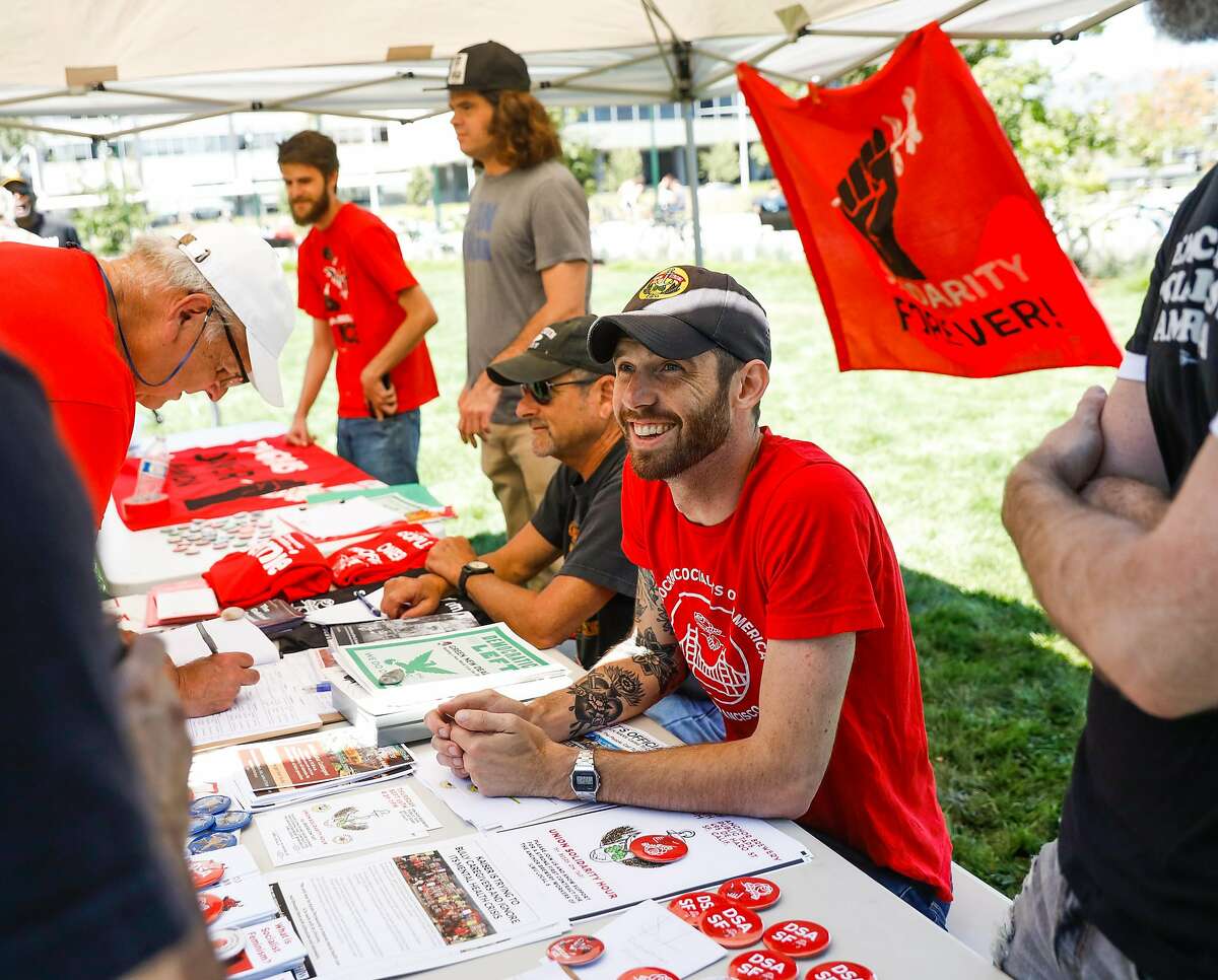 Evan McLaughlin (right) smiles as he chats with people at the Democrat Socialists of America booth at the Labor Day picnic in Oakland, California, on Monday, Sept. 2, 2019.