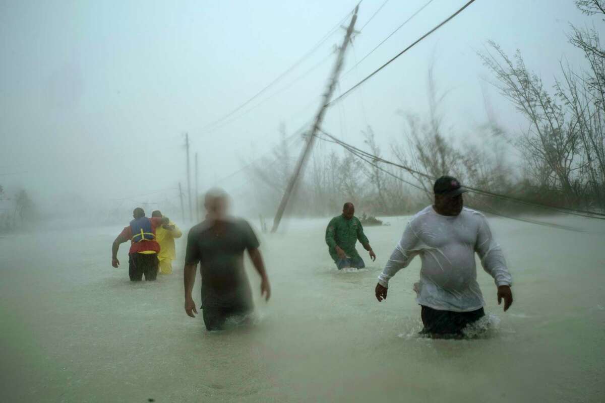 Volunteers walk under the wind and rain from Hurricane Dorian through a flooded road as they work to rescue families near the Causarina bridge in Freeport, Grand Bahama, Bahamas, Tuesday, Sept. 3, 2019. The stormas punishing winds and muddy brown floodwaters devastated thousands of homes, crippled hospitals and trapped people in attics. (AP Photo/Ramon Espinosa)