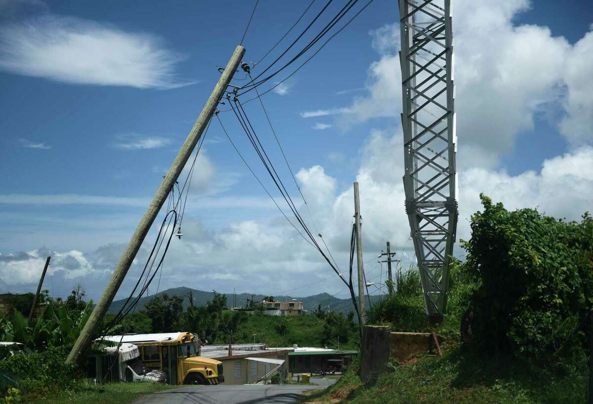 file - In this May 16, 2018 file photo, an electric power pole leans over the road in the Piedra Blanca area of Yabucoa, Puerto Rico, a town still mostly without power since it was struck by Hurricane Maria on Sept. 20. Puerto Rico’s new governor announced on Sunday, Aug. 11, 2019 that she is suspending an upcoming $450,000 contract to rebuild and strengthen the island’s power grid destroyed by Hurricane Maria. (AP Photo/Carlos Giusti, File)
