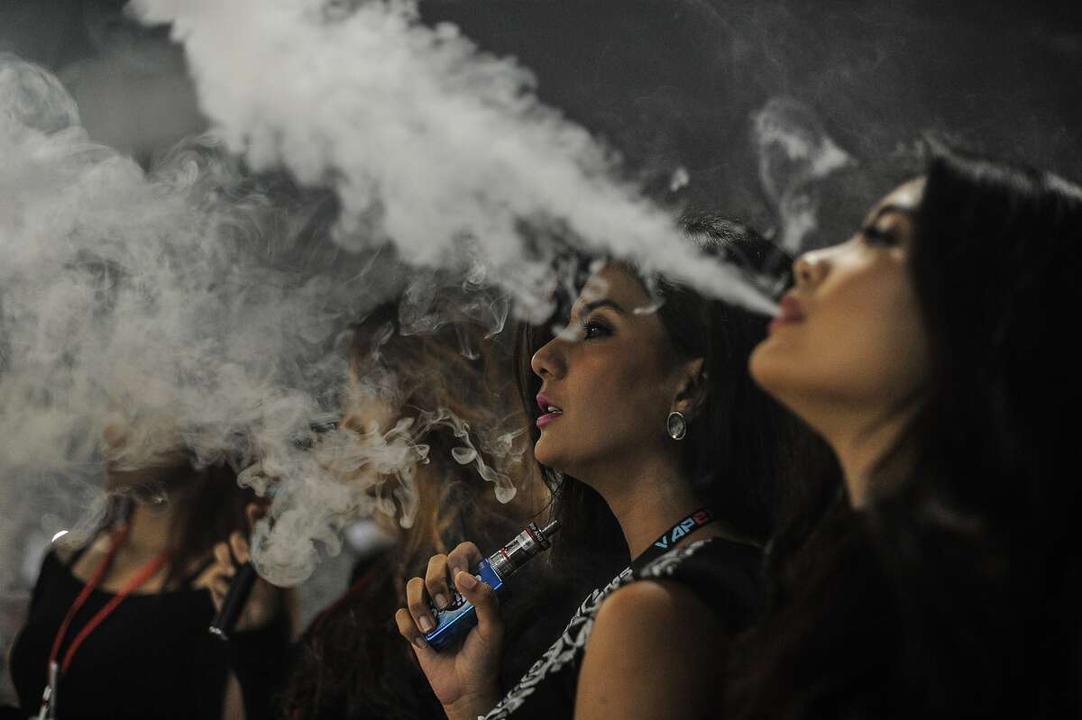 TO GO WITH Lifestyle-Malaysia-e-cigarette-tobacco-health,FEATURE by Satish Cheney This picture taken on December 5, 2015 shows promoters smoking electronic cigarettes during the Vape Fair in Kuala Lumpur. Vaping" is soaring in popularity in Malaysia, the largest e-cigarette market in the Asia-Pacific region, but authorities are threatening to ban the habit in for health reasons -- a move that has sparked anger from growing legions of aficionados. AFP PHOTO / MOHD RASFANMOHD RASFAN/AFP/Getty Images