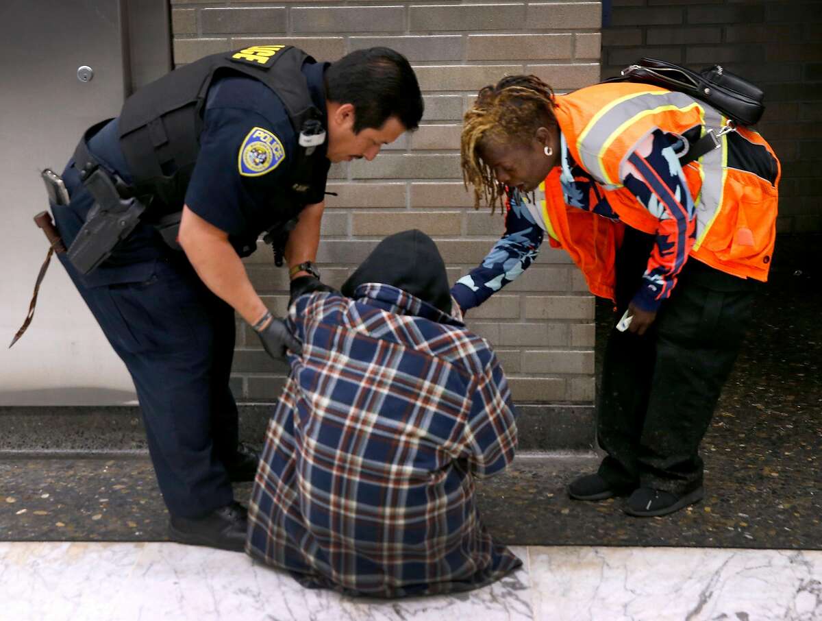A BART police officer, Rodney Berrera and a security guard, Cherie Pittman helps a transient get on his feet in a BART station on June 18, 2019. San Francisco agencies are considering a new policy targeting the 4,000 people who suffer from a combination of homelessness, mental illness, and substance abuse disorder.
