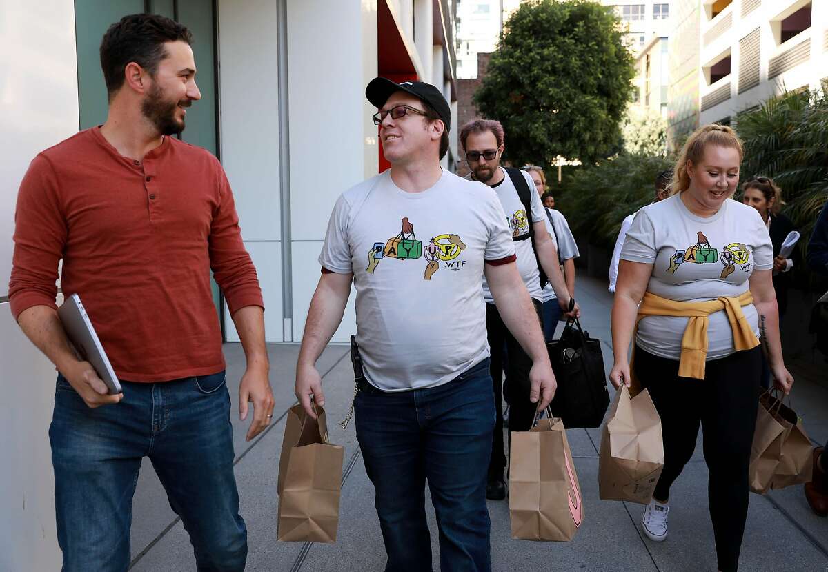 Keith Chapman, left, converses with Felix Sanchez, second from left, as Tyler Breisacher and Vanessa Bain walk with them outside of the Postmates headquarters at 201 Third St. in San Francisco, Calif., on Thursday, September 5, 2019. Workers from Postmates, DoorDash, and Instacart rallied outside these companies' corporate headquarters to deliver messages calling for new laws and policies. They also held bags of peanuts, since they say they are paid peanuts.